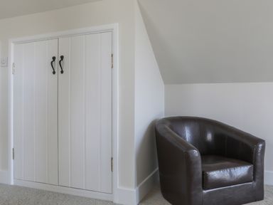 A small white cupboard with black handles next to a dark brown leather armchair in a corner of a room at Stable End Cottage in Malborough
