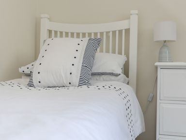 A bedroom with a white bed and polka dot bedding next to a white nightstand with a lamp at Stable End Cottage in Malborough