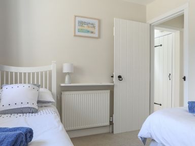 A bedroom with two single beds a lamp on a wall shelf and an open door at Stable End Cottage Malborough