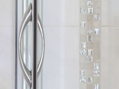 Close up of a metallic door handle on a glass door and a wall with small square reflective tiles at Stable End Cottage in Malborough