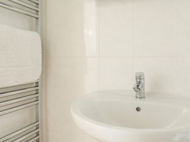A bathroom sink with a chrome faucet and a towel on a silver heated towel rail at Stable End Cottage in Malborough
