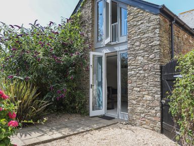 Stone exterior of a building with glass doors and windows open and plants surrounding at Stable End Cottage in Malborough