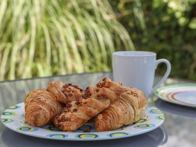 A plate with croissants and pastries next to a white mug on a glass table outdoors at Stable End Cottage in Malborough