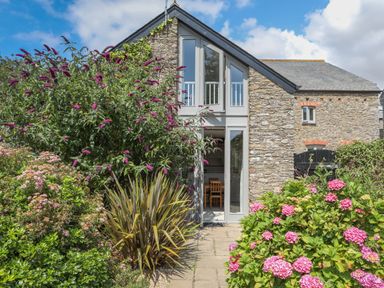 Stone exterior house with large glass doors and flowering garden at Stable End Cottage in Malborough