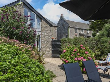 A garden with stone cottages bushes and outdoor chairs at Stable End Cottage in Malborough
