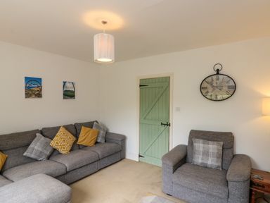 A living room with gray sofas and a green door with wall clock at 7 Dale End in Danby near Castleton