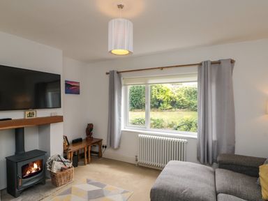 A living room with a wood burning stove a wall mounted television and a large window with curtains at 7 Dale End in Danby near Castleton