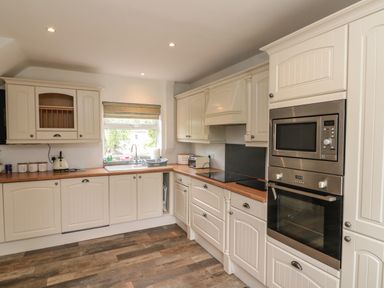 A kitchen with white cabinets a window above the sink and built in stainless steel microwave and oven at 7 Dale End in Danby near Castleton