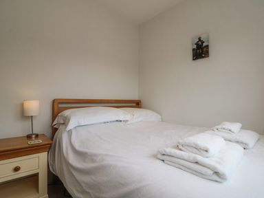 A bedroom with a double bed with white bedding and folded towels with a bedside table and lamp at 7 Dale End in Danby near Castleton