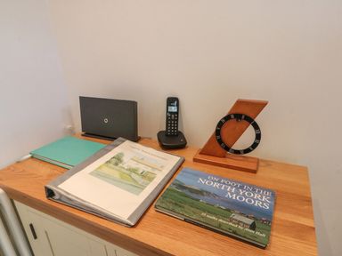 A wooden side cabinet with books folders a phone and a wooden clock at 7 Dale End in Danby near Castleton