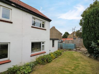 A backyard with grass and plants next to a white house with red roof tiles at 7 Dale End in Danby near Castleton