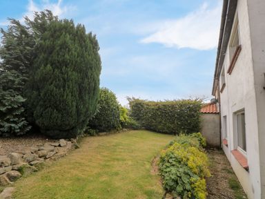 A garden with a lawn shrubs and a white house at 7 Dale End Danby near Castleton