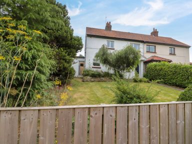 A fenced garden with grass and bushes in front of a semi detached house at 7 Dale End in Danby near Castleton