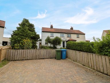 A paved driveway with two trash bins in front of a semi detached house with tiled roof and hedges at 7 Dale End in Danby near Castleton