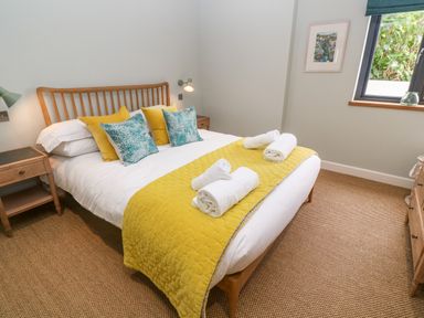 A bedroom with a wooden bed frame yellow quilt and rolled white towels on the bed at Postcard Lodge in Polruan