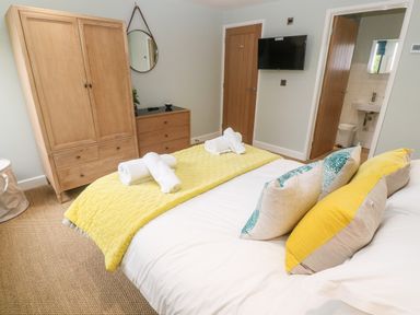 A bedroom with a bed with yellow and blue pillows and a yellow throw next to a wooden wardrobe and dresser at Postcard Lodge in Polruan