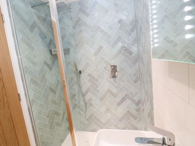 A bathroom shower with blue herringbone tiles and a glass door at Postcard Lodge in Polruan