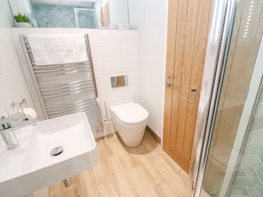 A bathroom with a sink and towel rack next to a toilet and wooden door at Postcard Lodge in Polruan