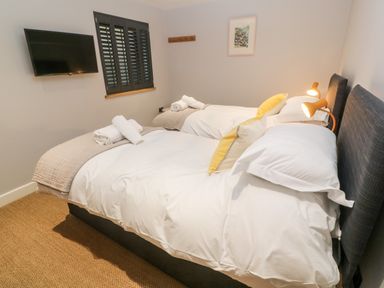 A bedroom with two single beds with white bedding and yellow pillows a wall mounted television and a window with shutters at Postcard Lodge in Polruan