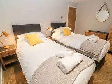 A bedroom with two single beds bedside tables with lamps and a round mirror at Postcard Lodge in Polruan