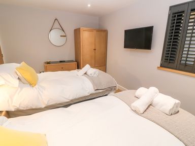 A bedroom with two beds a wooden wardrobe a wall-mounted television and a round mirror at Postcard Lodge in Polruan