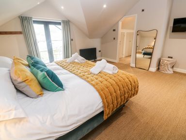 A bedroom with a bed with pillows and a throw a full-length mirror a television and a balcony door at Postcard Lodge in Polruan
