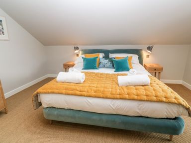 A bedroom with a bed with yellow quilt and teal pillows and two bedside tables with lamps at Postcard Lodge in Polruan