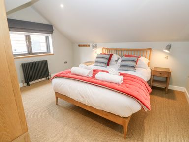 A bedroom with a wooden double bed with white and red bedding and two bedside tables at Postcard Lodge in Polruan
