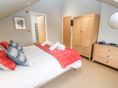 A bedroom with a bed red blanket and pillows wooden wardrobe and dresser with a mirror at Postcard Lodge Polruan