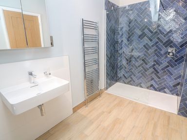 A bathroom with a sink a towel radiator and a shower with blue herringbone tiles at Postcard Lodge in Polruan