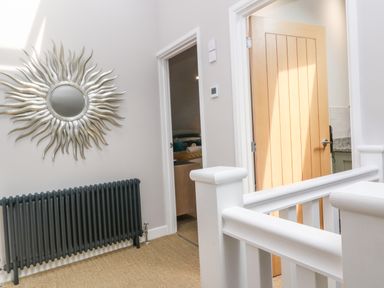 A hallway with a sunburst mirror above a dark radiator and two open doors at Postcard Lodge in Polruan