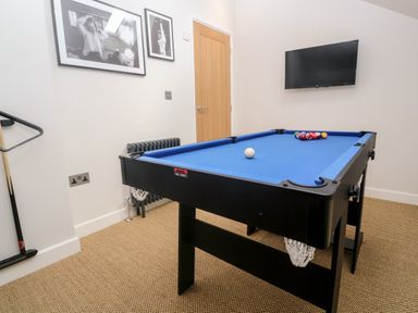 A pool table with blue felt and balls arranged on it in a game room with framed photos on the wall and a mounted TV at Postcard Lodge in Polruan