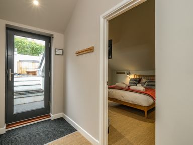 A hallway with a glass door leading outside and a view into a bedroom with a bed at Postcard Lodge in Polruan