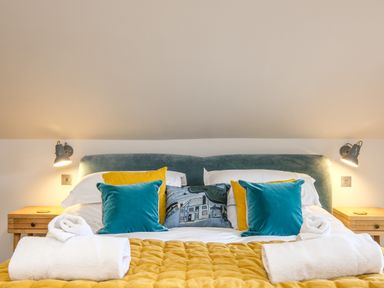 A bed with blue and yellow pillows a yellow quilt and rolled white towels at Postcard Lodge in Polruan