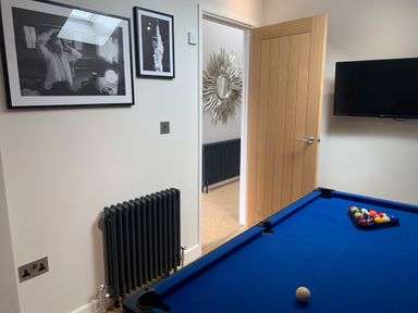 A room with a blue pool table a wall-mounted television and framed photographs on the wall at Postcard Lodge in Polruan
