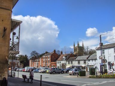 A street view with parked cars shops and a church tower in the background at The Hideaway in Eckington