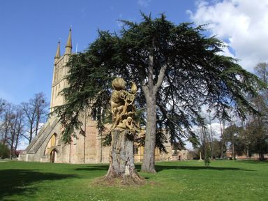 An outdoor scene with a carved wooden sculpture on a tree stump near a large tree and a church in the background
