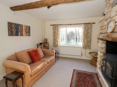 A living room with a patterned sofa red cushion wooden side tables stone fireplace and a window with floral curtains at The Hideaway in Eckington