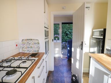 A kitchen with a gas stove oven microwave and refrigerator with a view through an open door to an outdoor patio with chairs at The Hideaway in Eckington