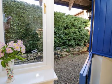 A small garden area with gravel ground two chairs a stone wall and green bushes viewed through a white window and blue door at The Hideaway in Eckington