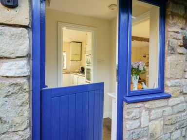 A blue half door leading to a kitchen with white cabinets and a window at The Hideaway in Eckington