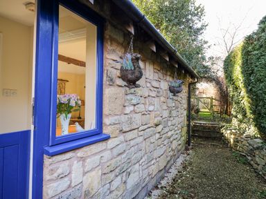 A stone exterior wall with a blue door and window two hanging bird planters a gravel path and garden gate at The Hideaway in Eckington
