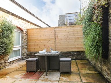 An outdoor patio with a small table and two chairs with cushions against stone walls and wooden fencing at Rock House Trebarwith Strand near Tintagel
