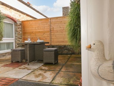 A small outdoor patio with a wicker table and stools set with plates and glasses at Rock House Trebarwith Strand near Tintagel