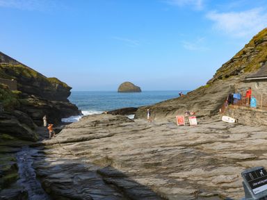 A rocky coastal area with people walking and an island in the sea at Rock House in Trebarwith Strand near Tintagel