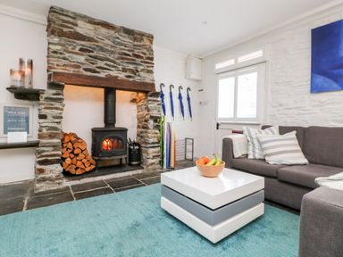 A living room with a stone fireplace a gray sofa striped cushions a modern white coffee table with fruit and a blue rug at Rock House Trebarwith Strand near Tintagel