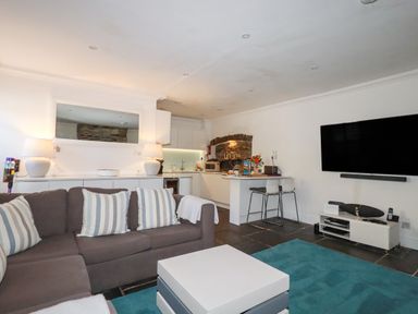 A living room with a sofa and kitchen area at Rock House in Trebarwith Strand near Tintagel