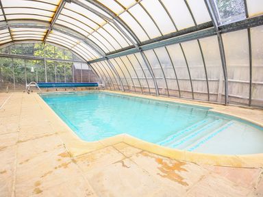 An indoor swimming pool with steps and a retractable cover in a curved glass enclosure at Stone Wheel Cottage in Hook Norton