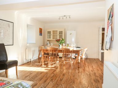 A dining room with a wooden table and chairs a cabinet a fridge and a bulletin board at Stone Wheel Cottage in Hook Norton