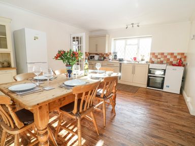 A kitchen with a wooden dining table set with plates and glasses and white cabinets at Stone Wheel Cottage in Hook Norton